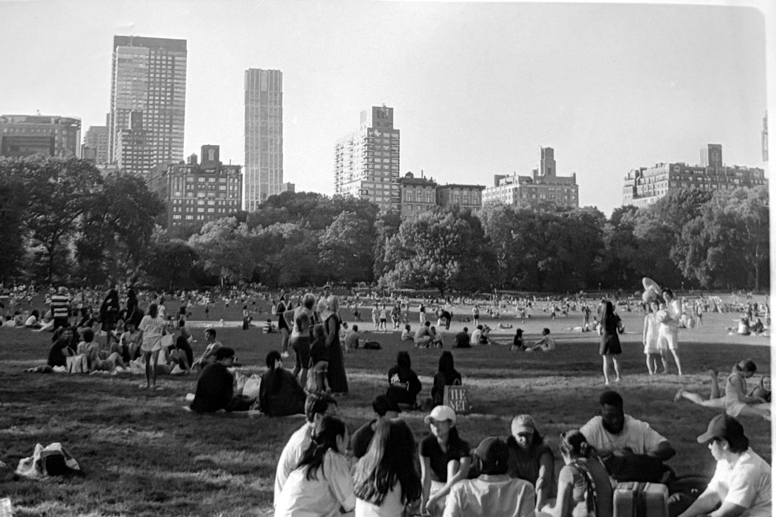 Black and white photograph of a crowded park lawn with a city skyline behind it.