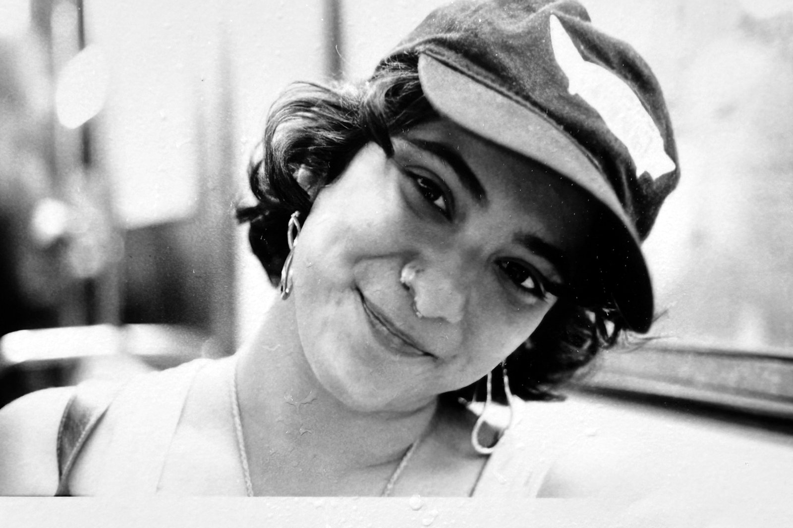 Black and white portrait of a woman in a peaked cap, smiling, shot close through glass.
