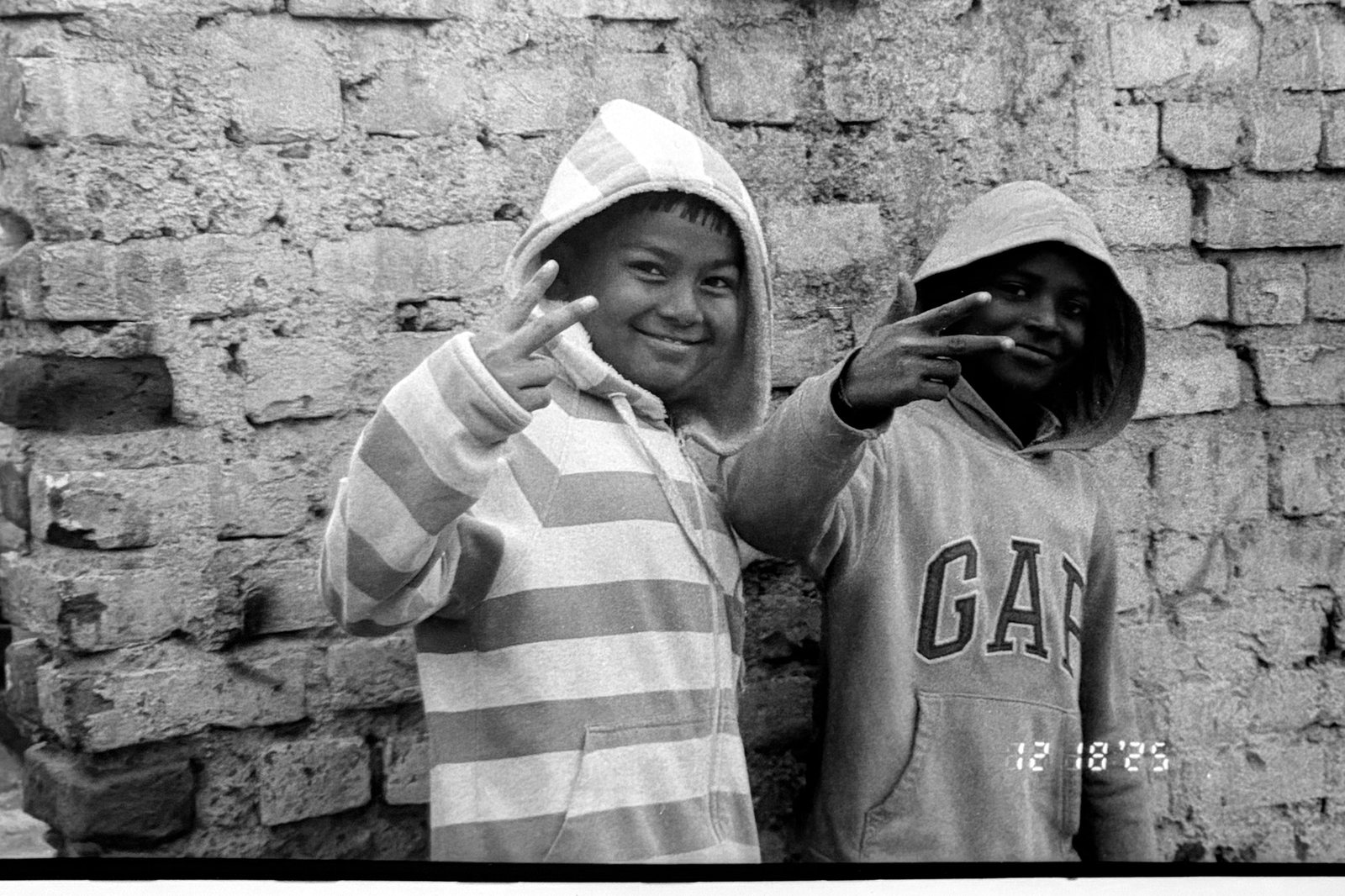 Black and white photograph of two children in hooded sweatshirts against a brick wall.