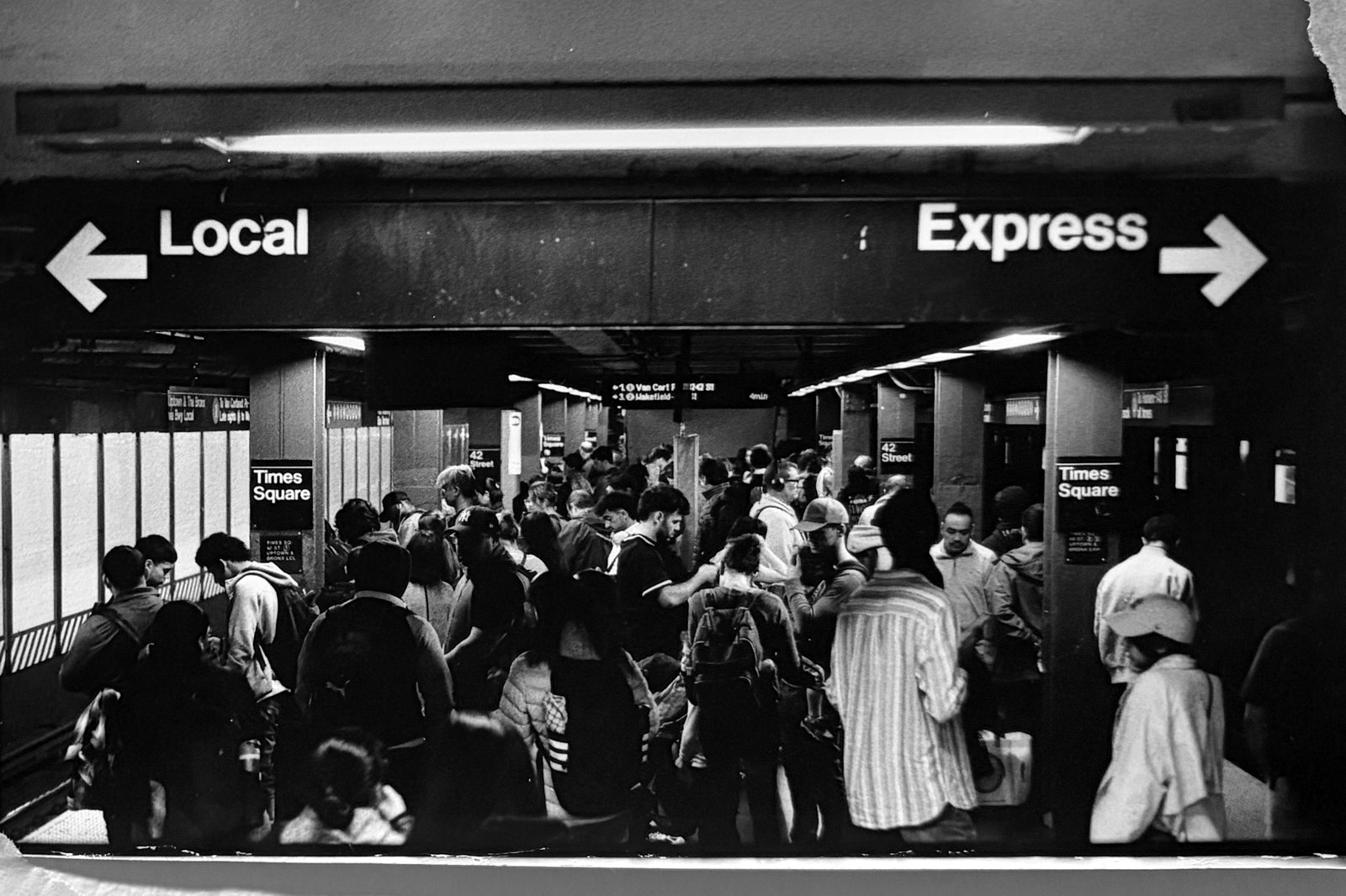 Black and white photograph of a subway concourse under signs reading Local and Express.