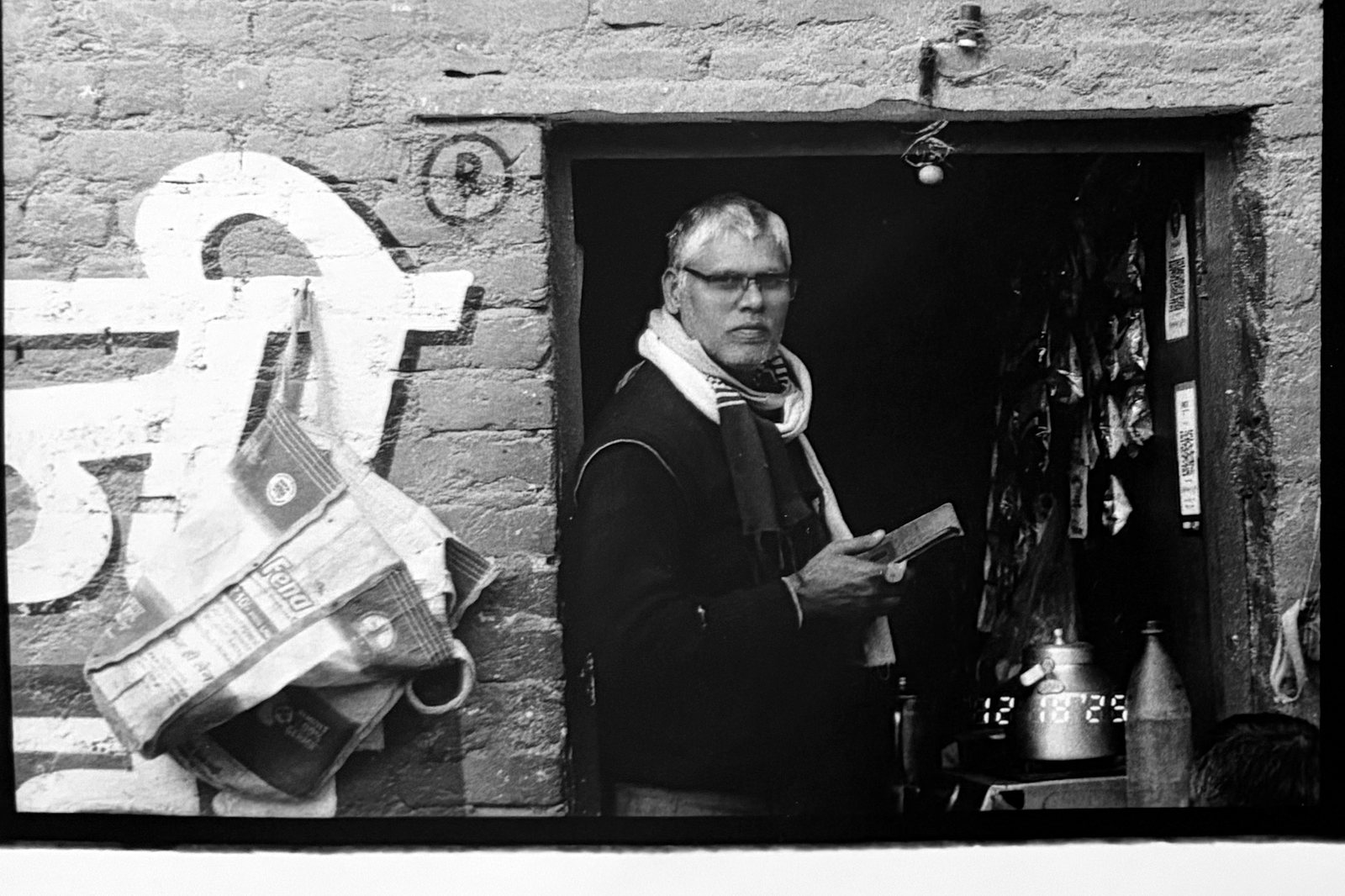 Black and white photograph of a man reading in a doorway beside a painted brick wall.
