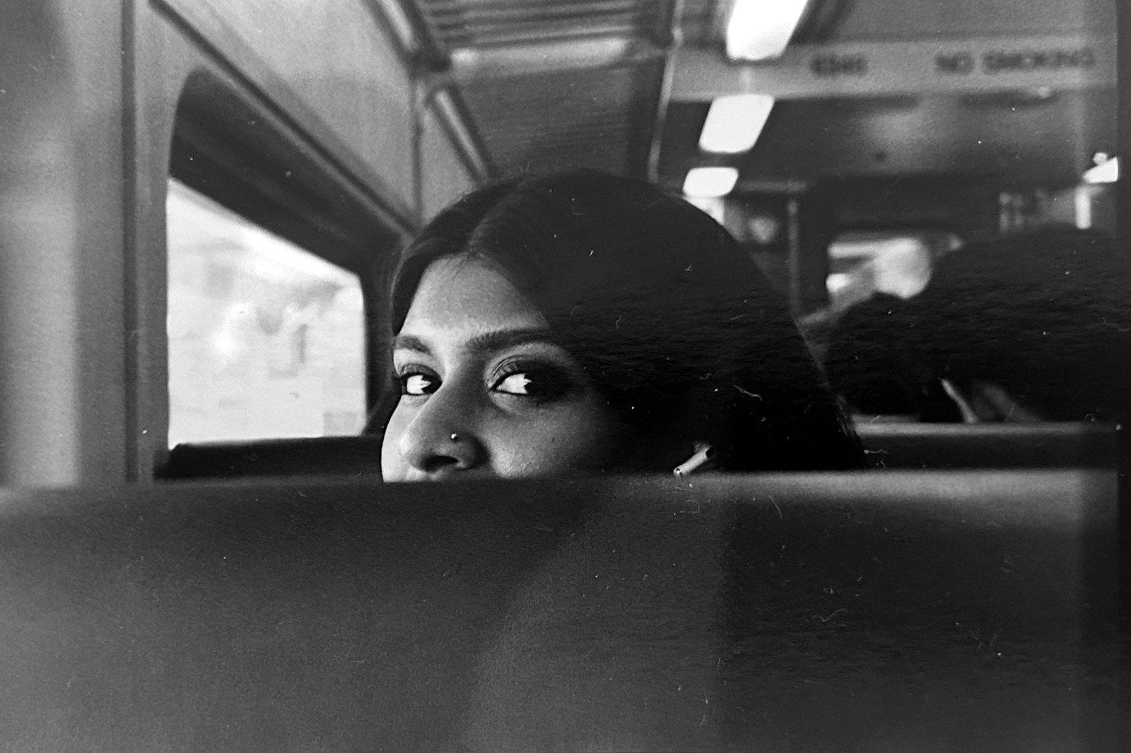 Black and white photograph of a woman looking back over a seat inside a train car.